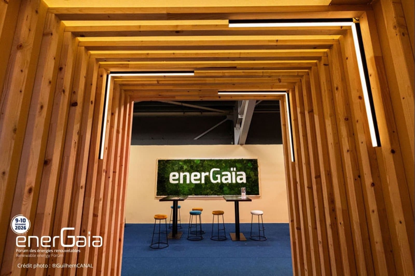 Wooden meeting area at the EnerGaïa Forum, with the green wall bearing the show logo
